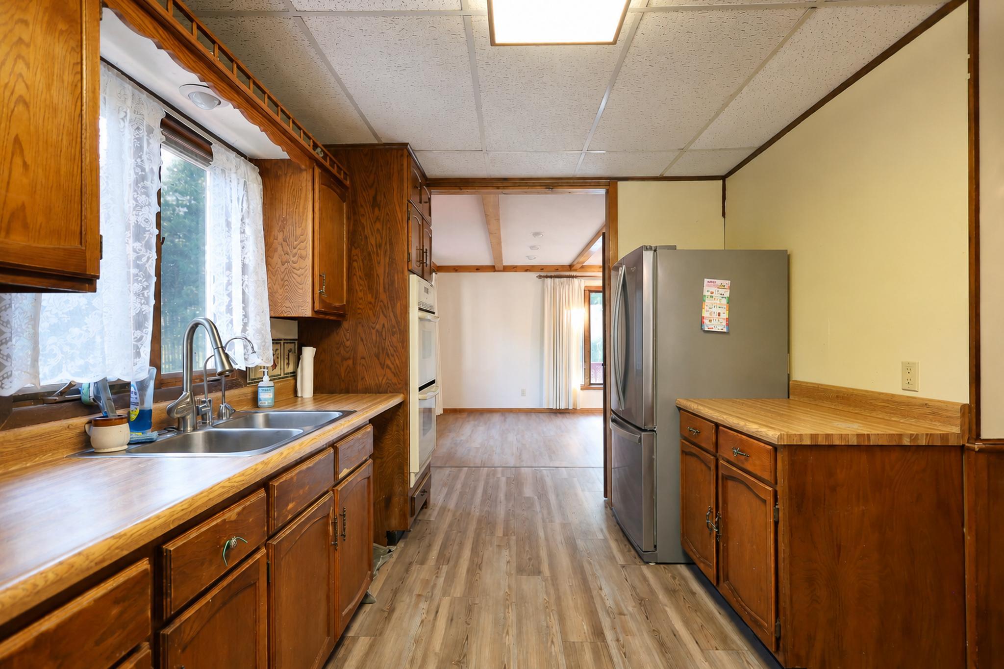 Kitchen with dark wood cabinets, a double sink, and a stainless steel refrigerator beside an open doorway.