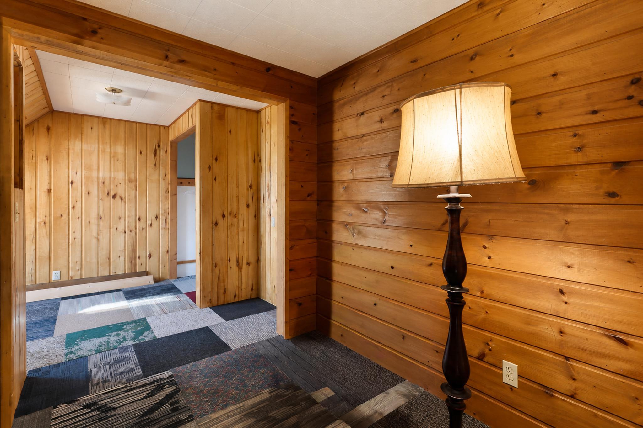 Wood-paneled entry hall with a tall floor lamp, patchwork carpet, and open doorway.