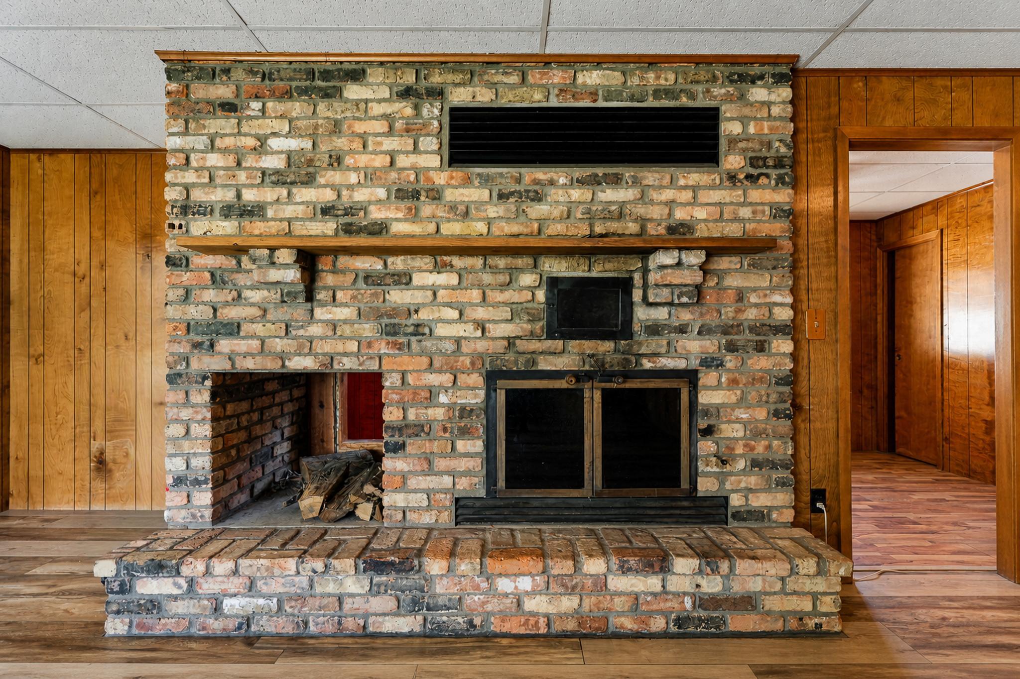 Brick fireplace with a raised hearth and wood mantel in a wood-paneled room.