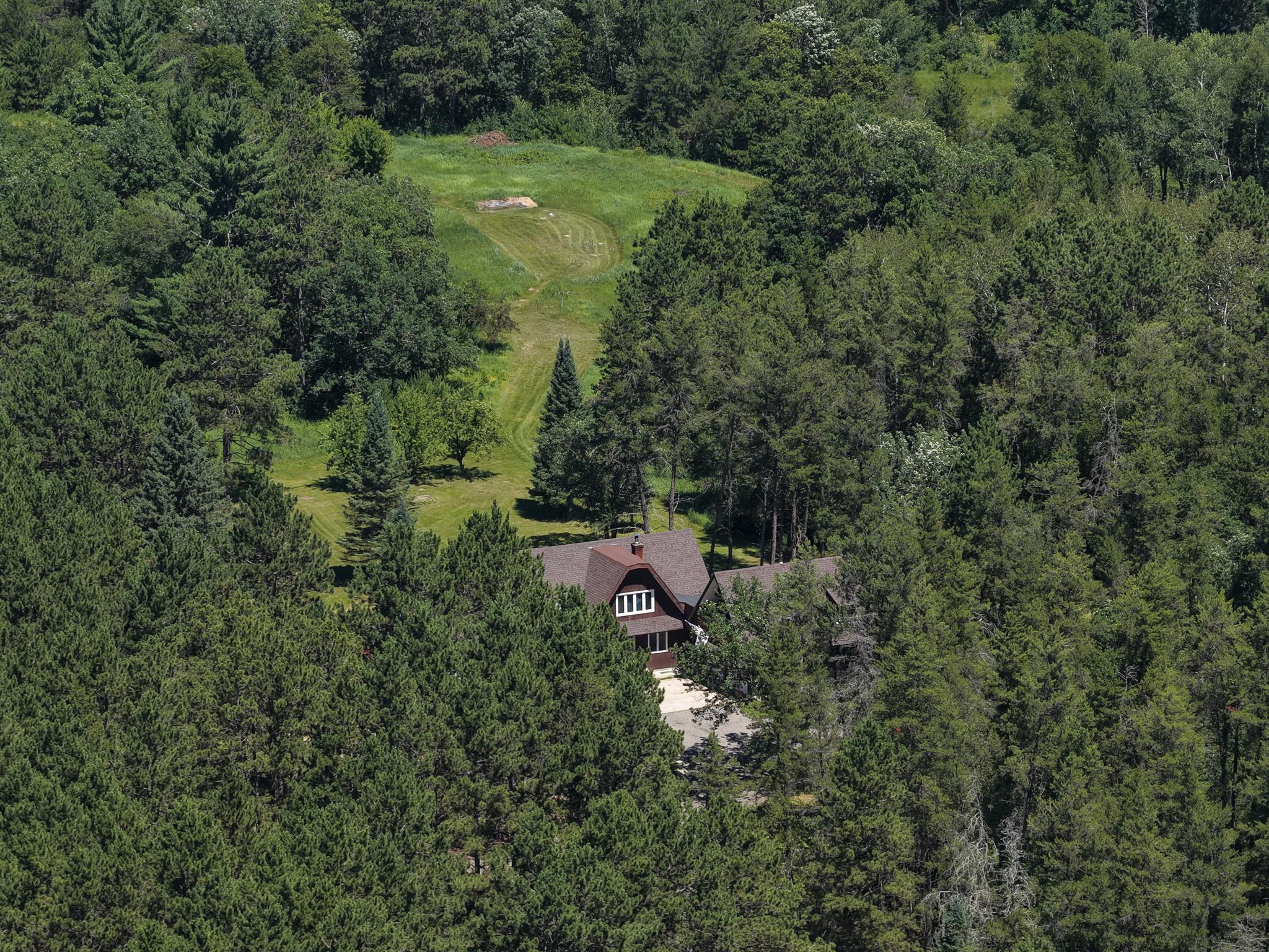 Aerial view of a house nestled in dense woods beside a long grassy clearing.