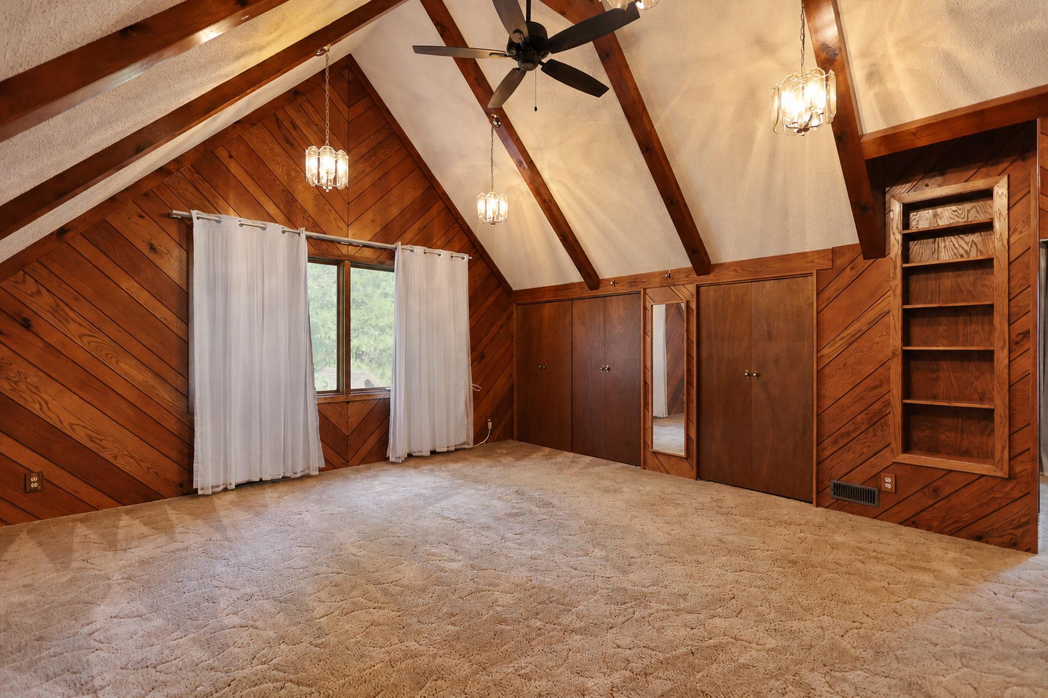 Vacant vaulted bedroom with wood-paneled walls, exposed beams, and built-in shelving.
