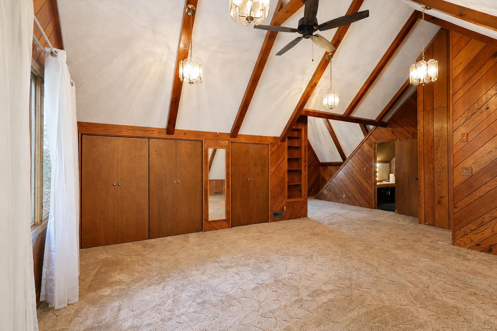 Bedroom with a vaulted beam ceiling, wood-paneled walls, built-in closets, and beige carpet.