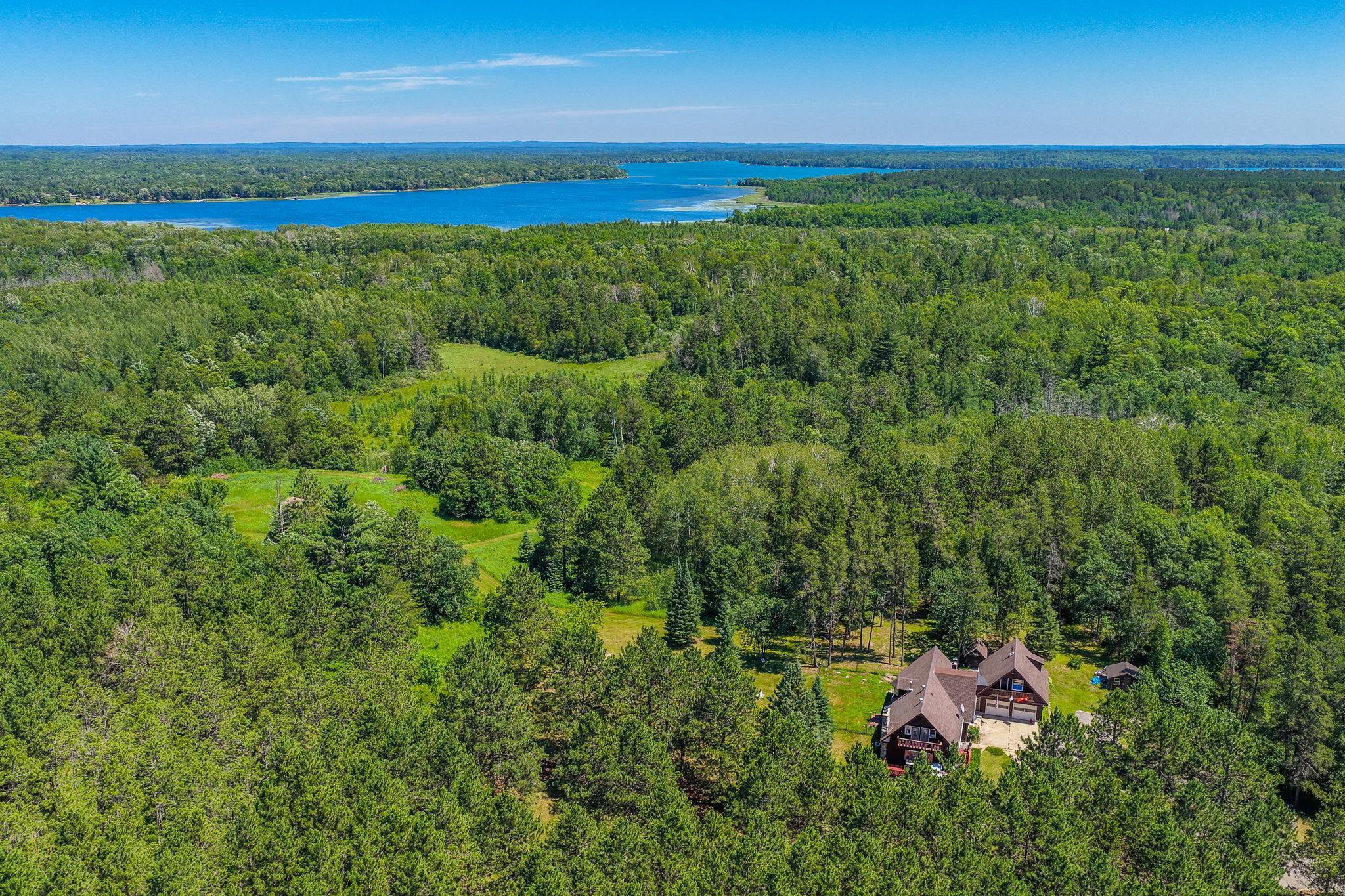 Aerial view of a wooded home near a lake, with a clearing and small outbuilding.