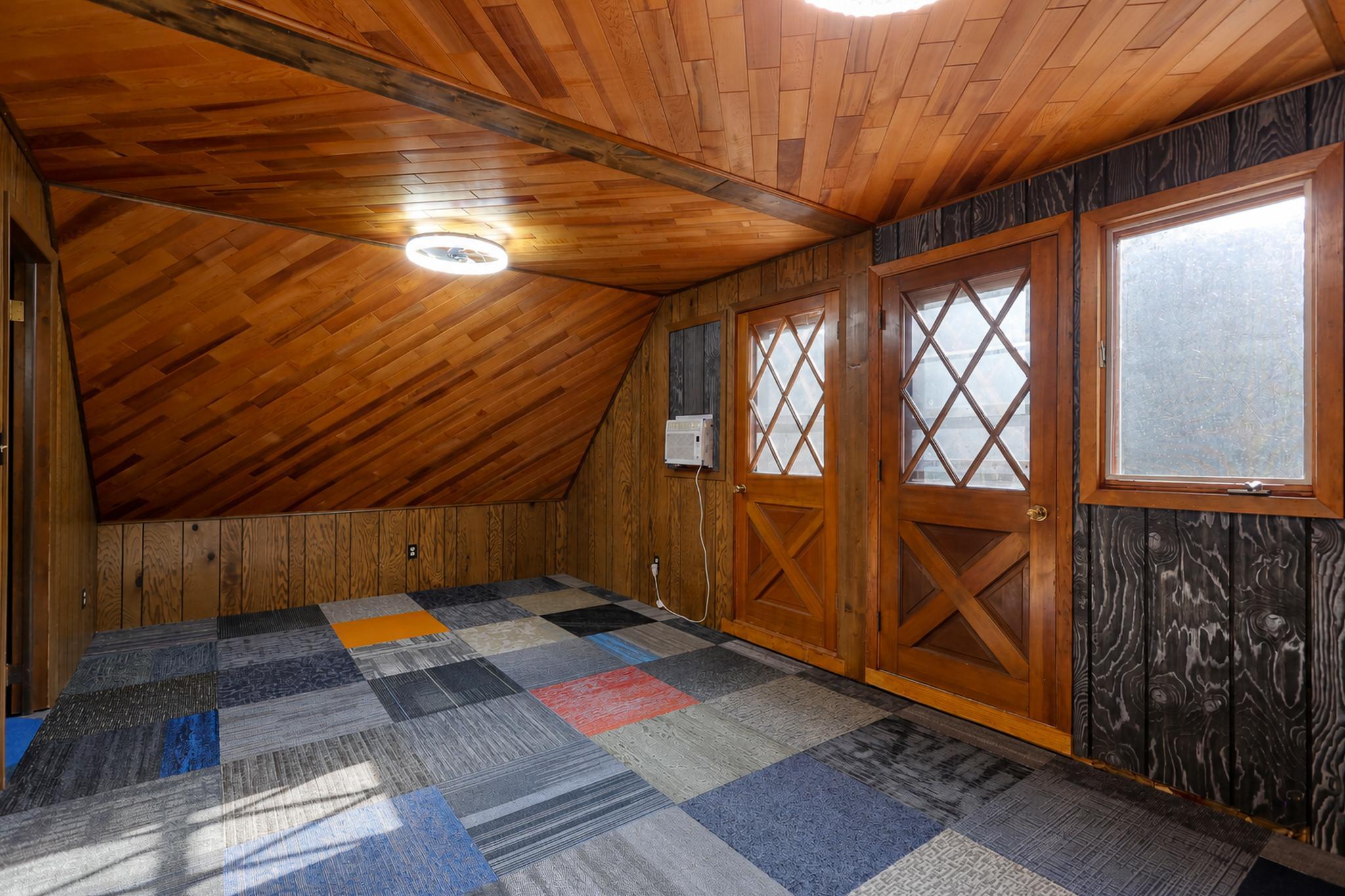 Empty room with patchwork carpet, sloped wood ceiling, and two diamond-windowed wooden doors.