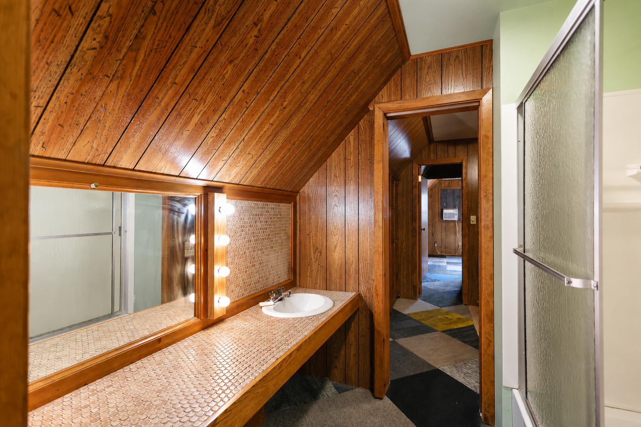 Bathroom with a long tiled vanity, illuminated mirror, and glass shower beneath a vaulted wood ceiling.
