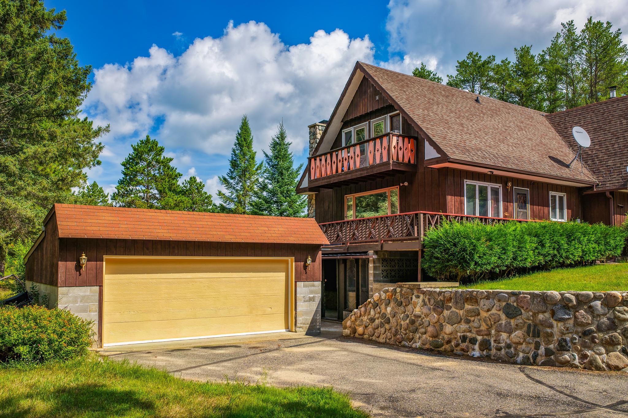 Chalet-style home with a red-trimmed balcony, yellow garage door, and stone retaining wall.