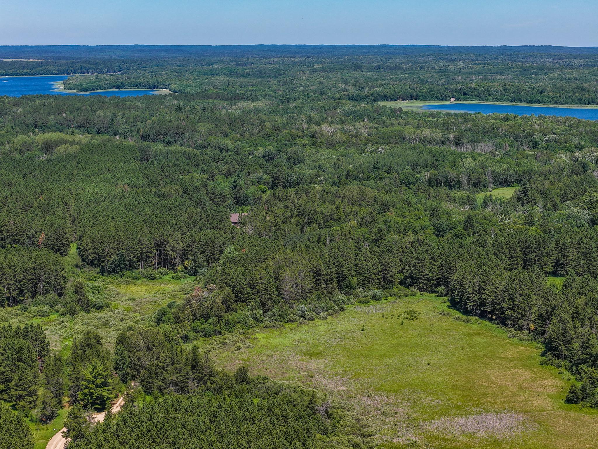 Aerial view of wooded acreage with a grassy clearing, a small building, and distant lakes.