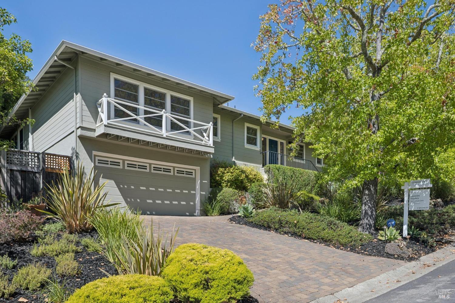 Two-story gray-green home with a white balcony, landscaped yard, and paved driveway.