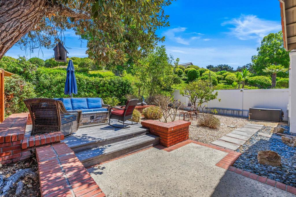 Backyard patio with blue-cushioned seating, a raised wooden deck, and landscaped garden beds.
