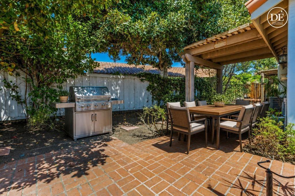 Backyard patio with a stainless-steel grill and dining set beneath a wooden pergola.