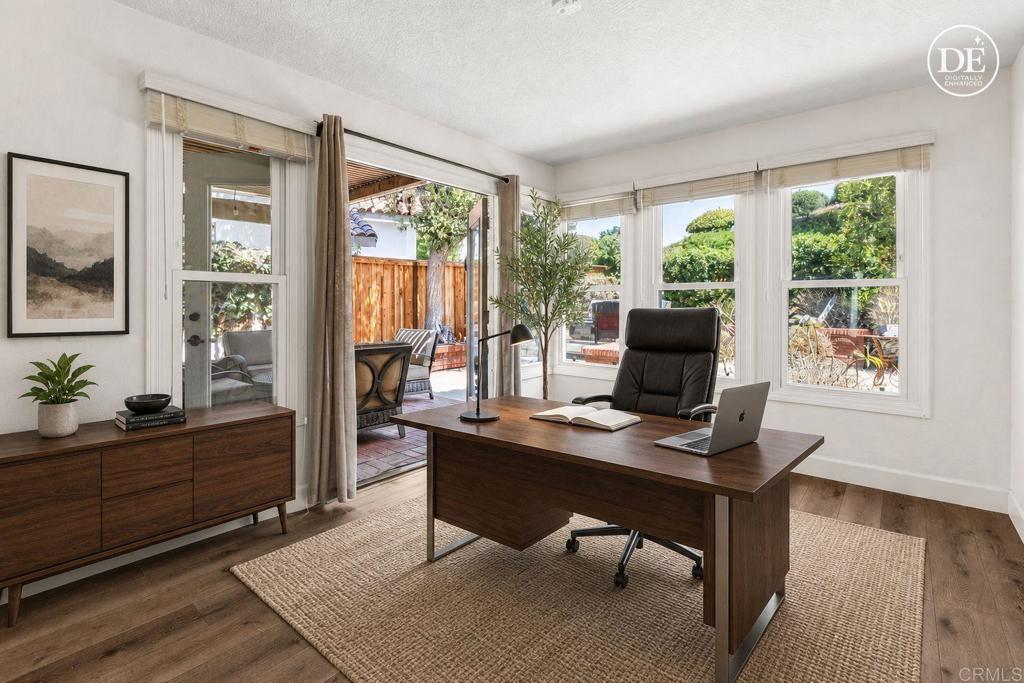 Furnished home office with a dark wood desk, large windows, and an open door to a patio.