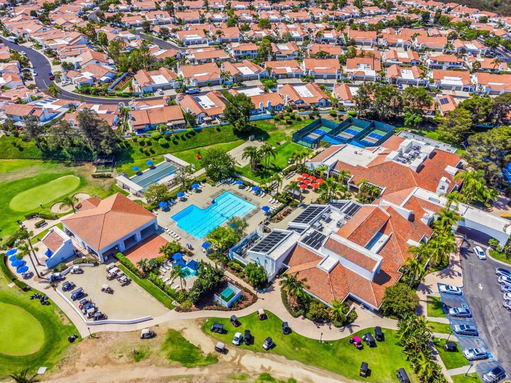 Aerial view of a residential community with a pool, tennis courts, and neighboring golf course.