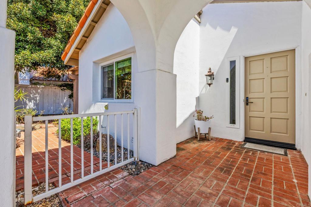 Home entrance with a white stucco arch, tan paneled door, and red brick patio.