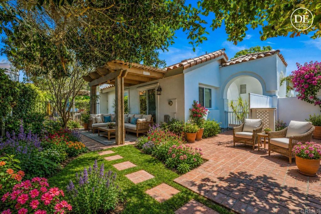 Landscaped backyard patio with a wooden pergola, brick paving, flower beds, and wicker seating.