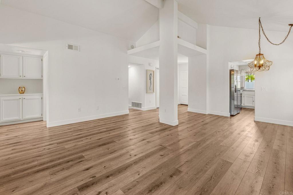 Vacant open living and dining area with wide-plank wood flooring and a brass chandelier.