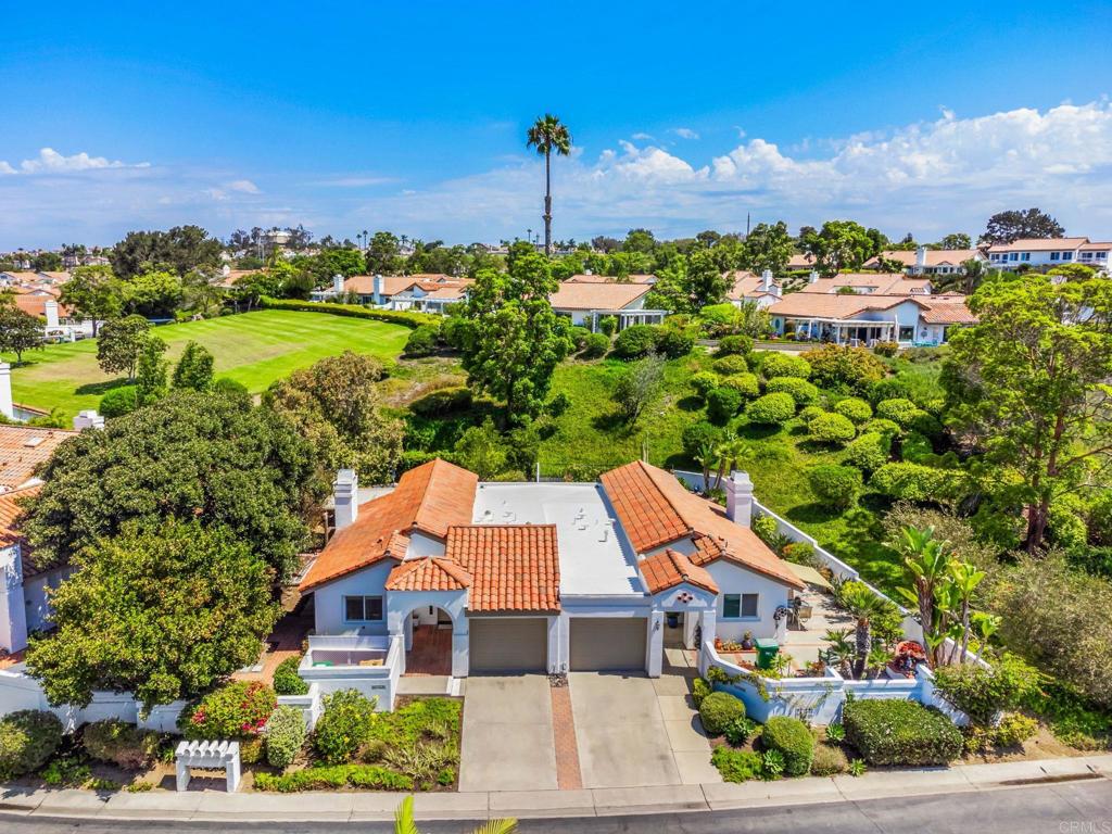 Aerial view of a single-story home with a terracotta roof, landscaped yard, and broad green space nearby.