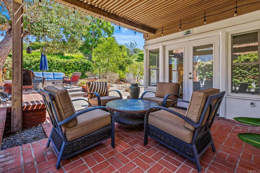 Outdoor patio with brick flooring, pergola, cushioned seating, and garden views.