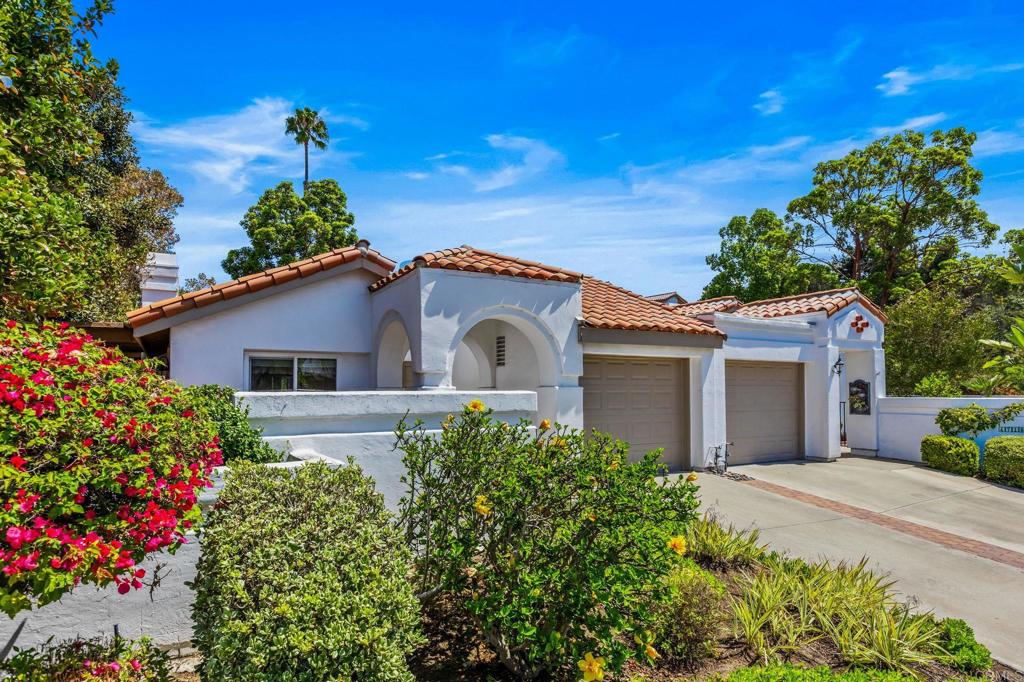 White stucco home with red tile roof, arched entry, and two-car garage framed by flowering gardens.