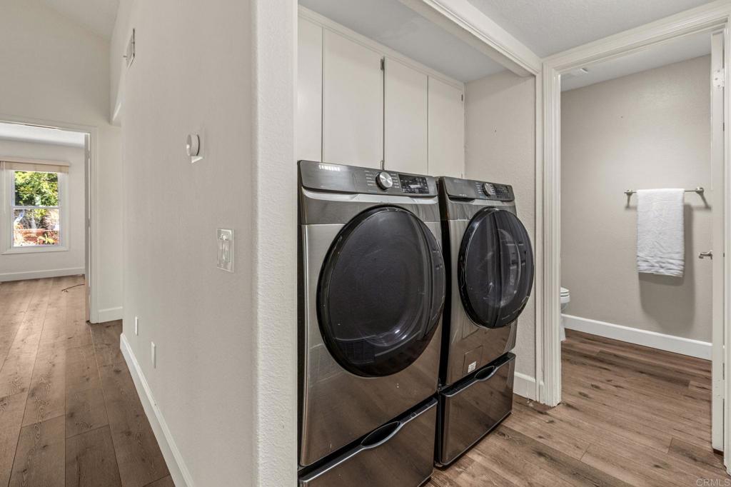 Laundry area with two stainless-steel front-loading machines and wood-look flooring.