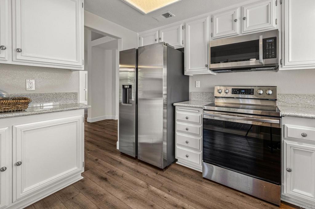 Kitchen with white cabinets, stone counters, stainless appliances, and brown wood-look flooring.