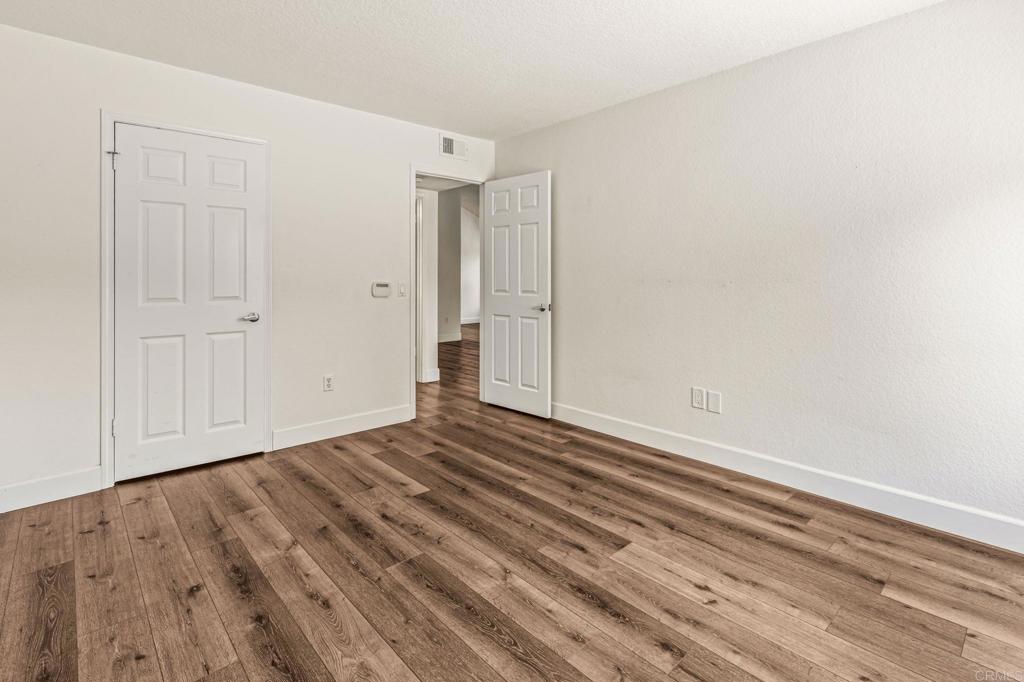 Empty room with wide-plank wood floors and an open door to the hallway.