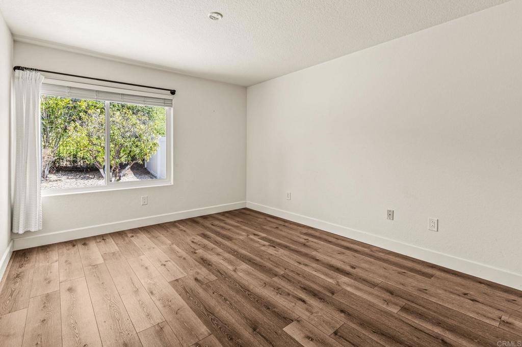 Empty bedroom with wood-look plank flooring and a window overlooking a leafy yard.