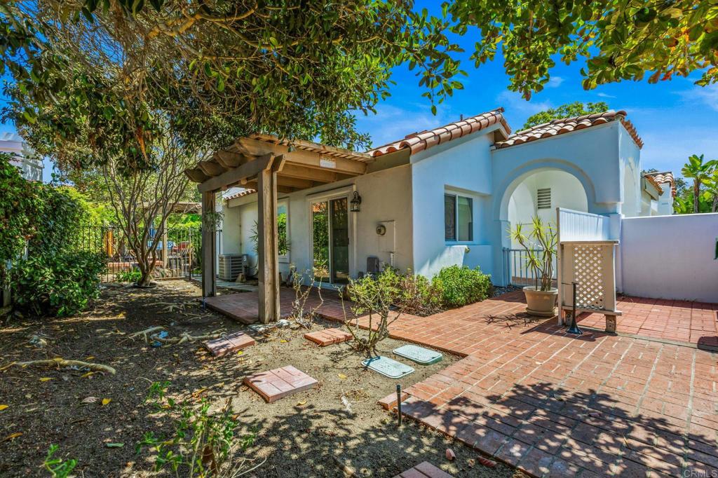 Back of a light-blue stucco home with an arched balcony, covered patio, and brick terrace.