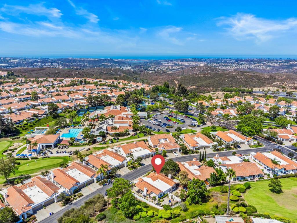 Aerial view of the home among tiled-roof houses, with pools and ocean on the horizon.