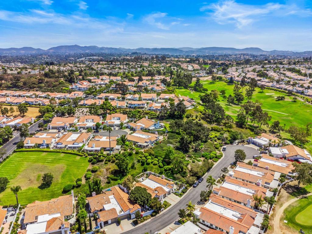Aerial neighborhood view with terracotta-roofed homes, a golf course, and distant hills.