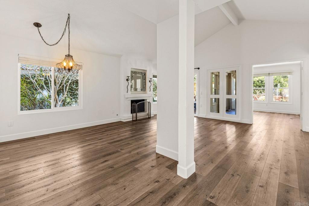Empty living room with wide-plank wood floors, a fireplace, chandelier, and French doors.