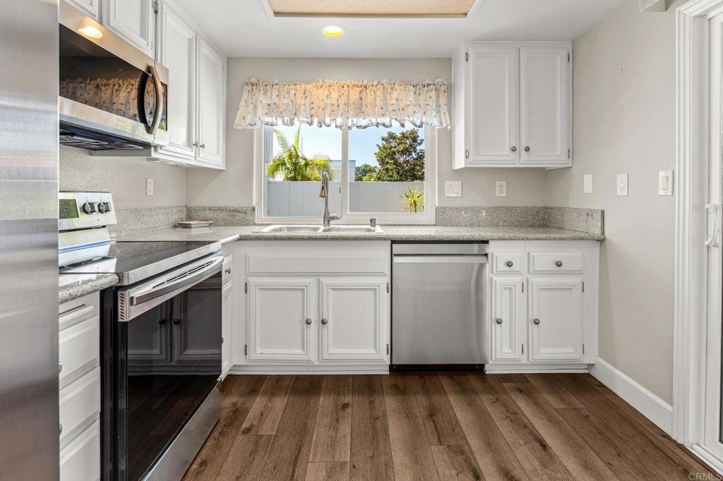 Kitchen with white cabinets, granite counters, stainless steel appliances, and a window above the sink.