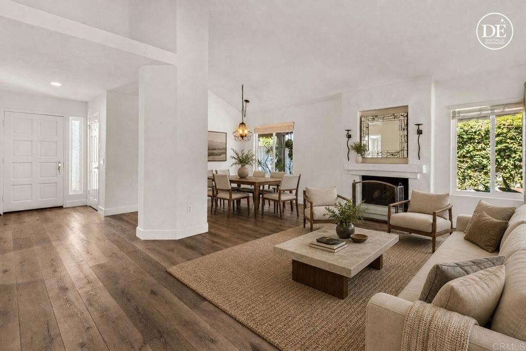 Staged living and dining room with a beige sectional, stone coffee table, fireplace, and wide-plank wood floors.