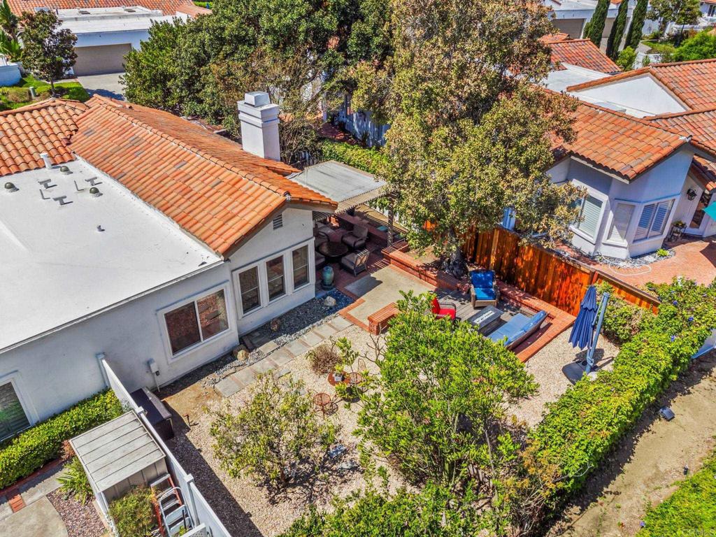 Aerial view of a home’s backyard with a covered patio, outdoor seating, and mature trees.
