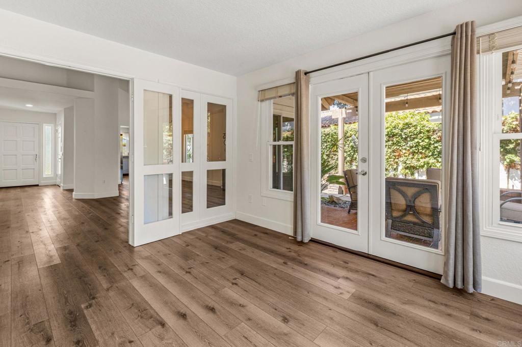 Empty room with wide-plank wood floors and French doors opening to a covered patio.