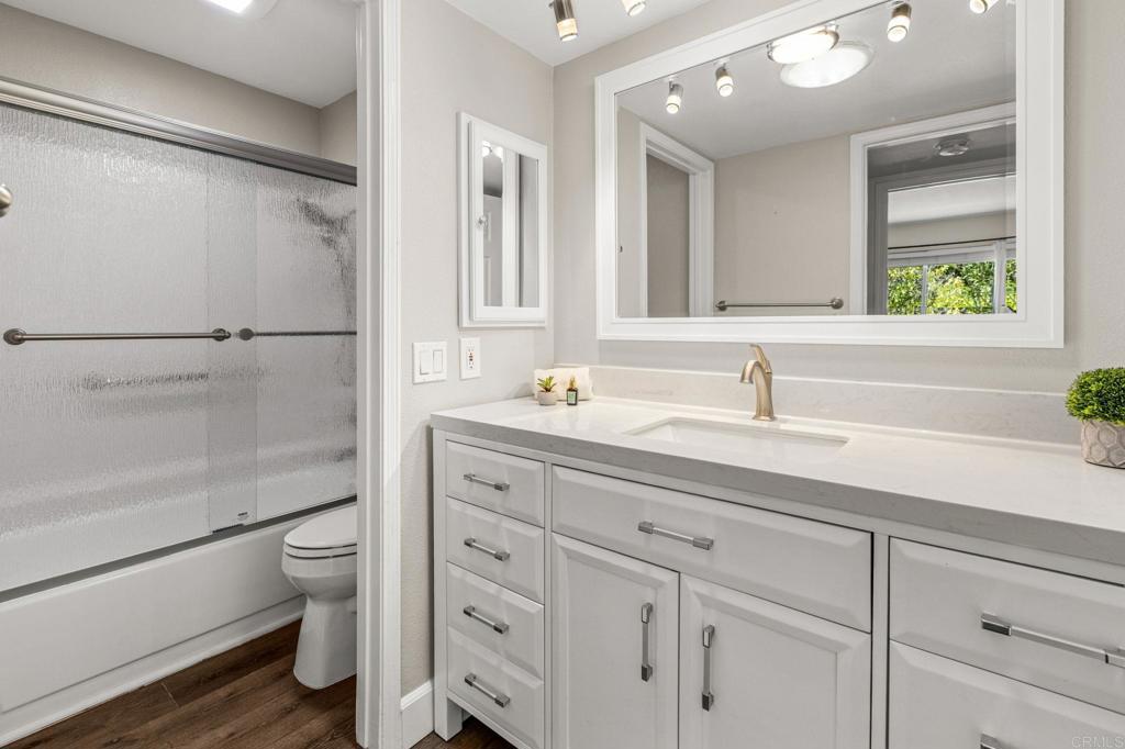 Bathroom with a long white vanity and framed mirror beside a frosted-glass tub and shower.