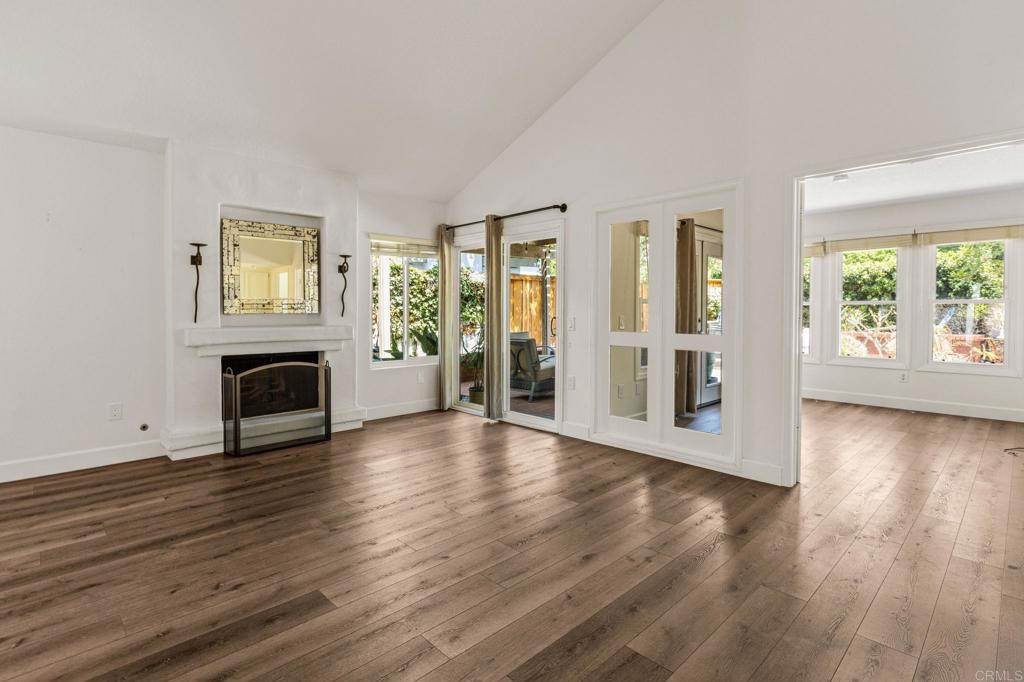 Vacant living room with a white fireplace, wide-plank wood floors, and glass doors overlooking greenery.