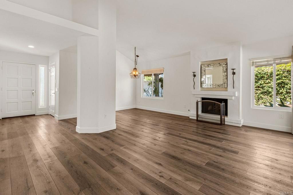 Empty living room with wide-plank wood floors and a fireplace beneath a mirrored mantel.