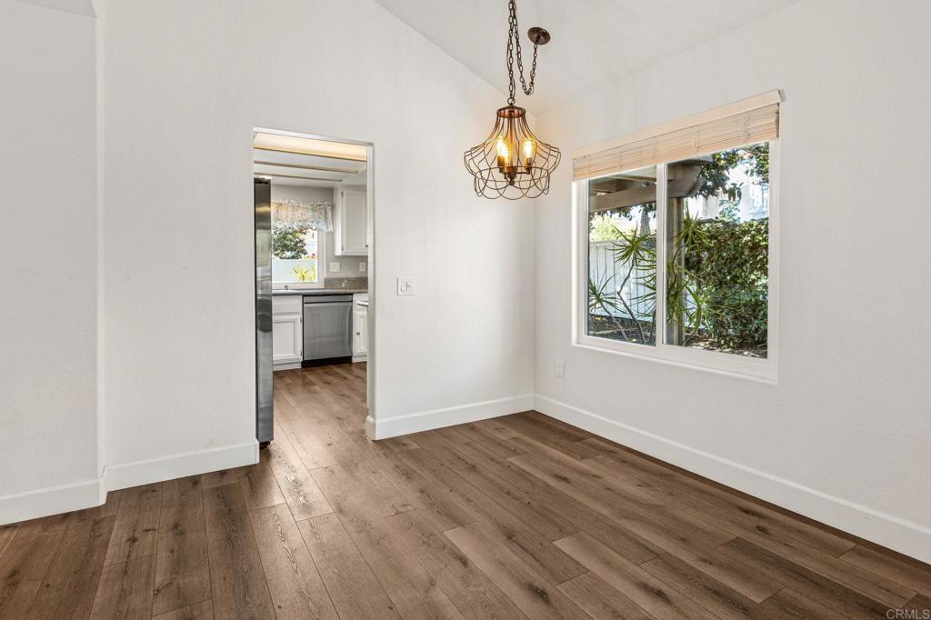 Empty dining room with wide-plank wood floors, a hanging pendant light, and a large window overlooking greenery.