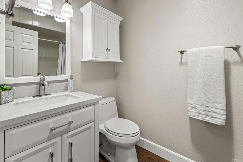 Bathroom with a white vanity, toilet, wall cabinet, and folded towel.