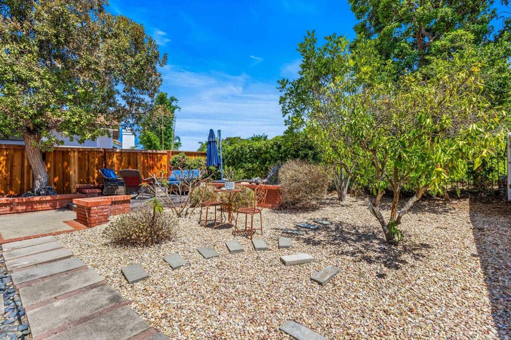 Gravel backyard with mature trees, stepping stones, and a patio seating area beside a wooden fence.