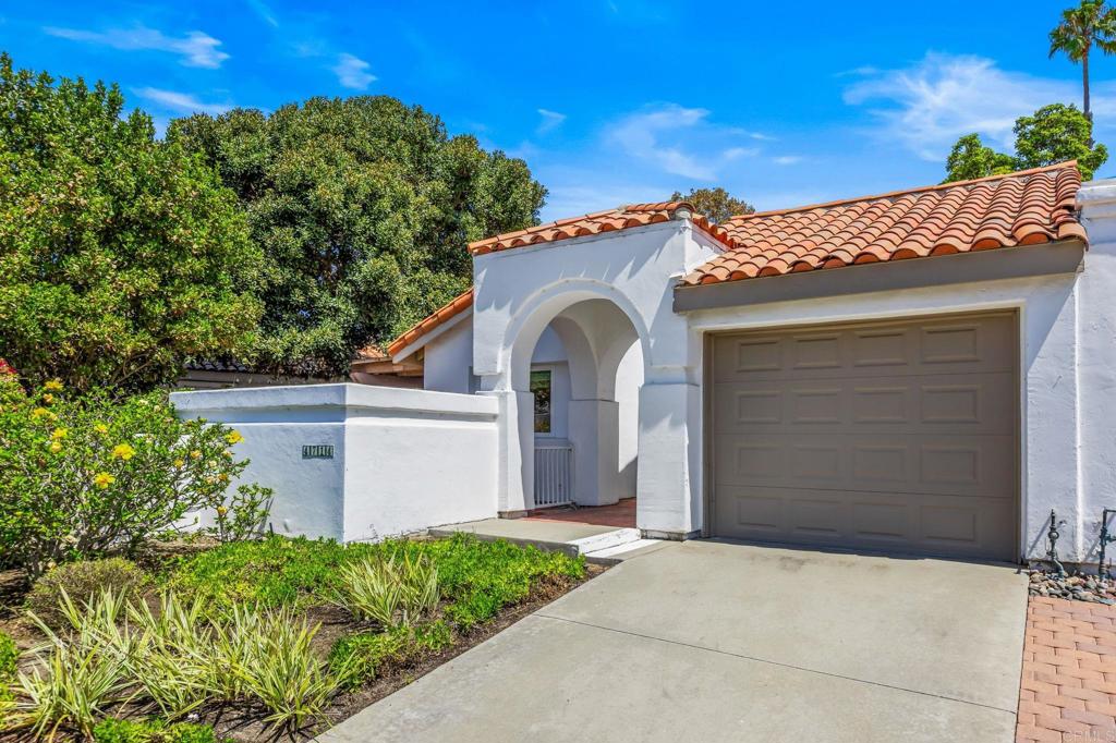 White stucco home with a terracotta tile roof, arched entry, and attached garage.