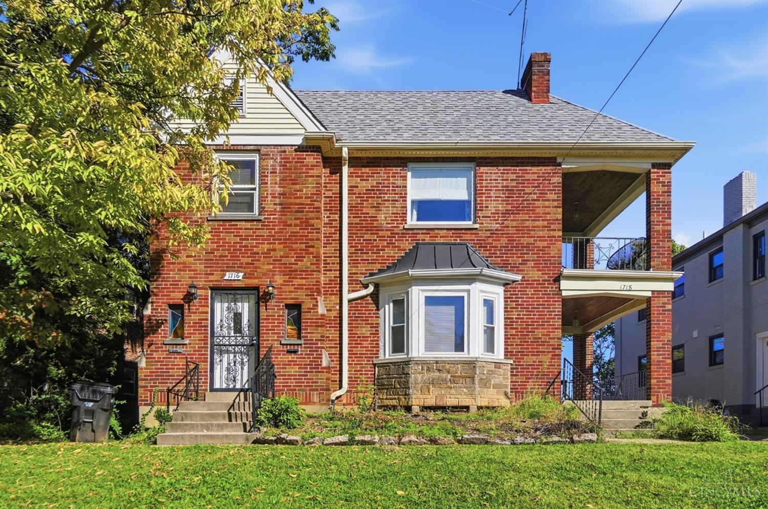 Red-brick home with a white-trimmed bay window, covered porch, and front lawn.