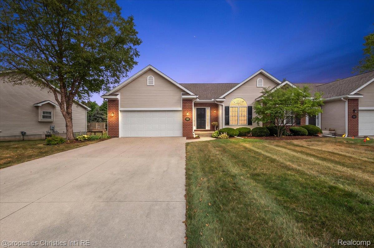 Home exterior with attached garage, broad driveway, brick accents, and an illuminated front window.