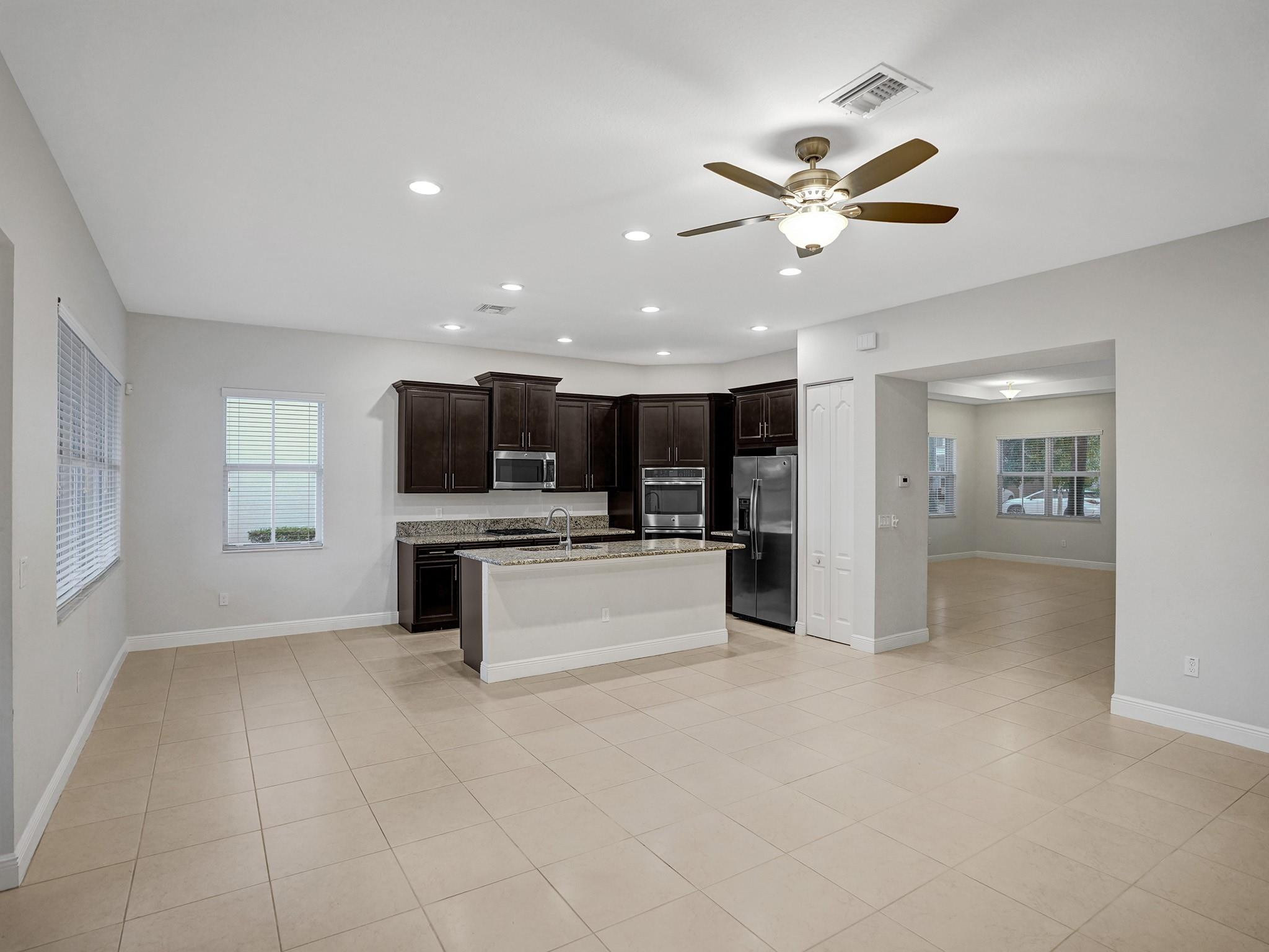 Kitchen with dark cabinets, granite island, stainless steel appliances, and beige tile floors.