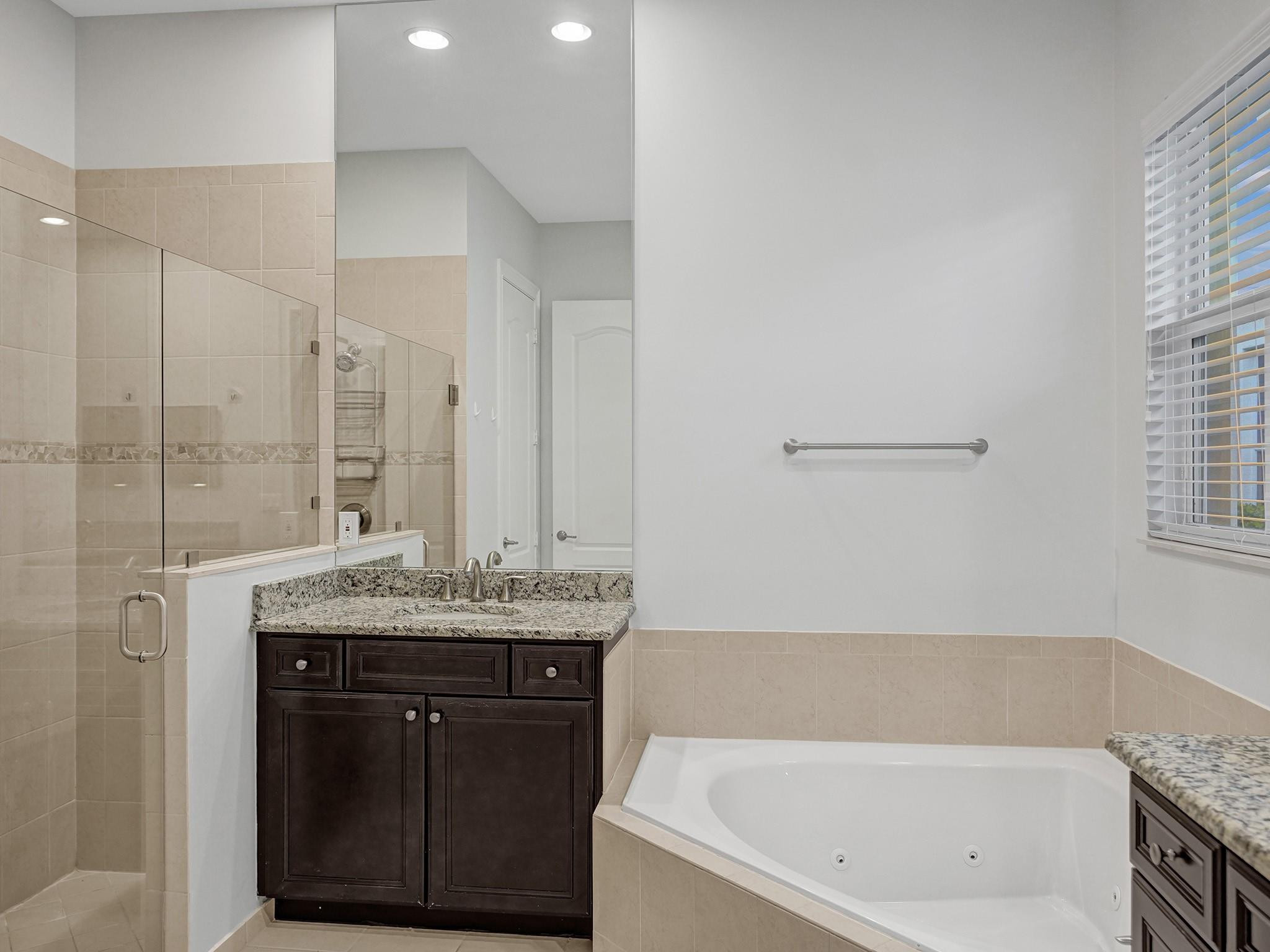 Bathroom with a glass shower, jetted corner tub, and dark wood granite-topped vanity.