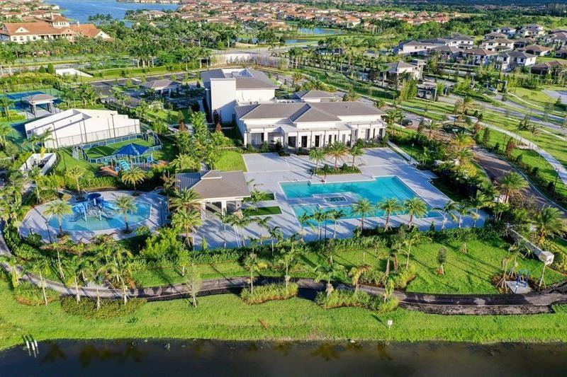 Aerial view of a community clubhouse, pools, tennis courts, and surrounding homes beside waterways.