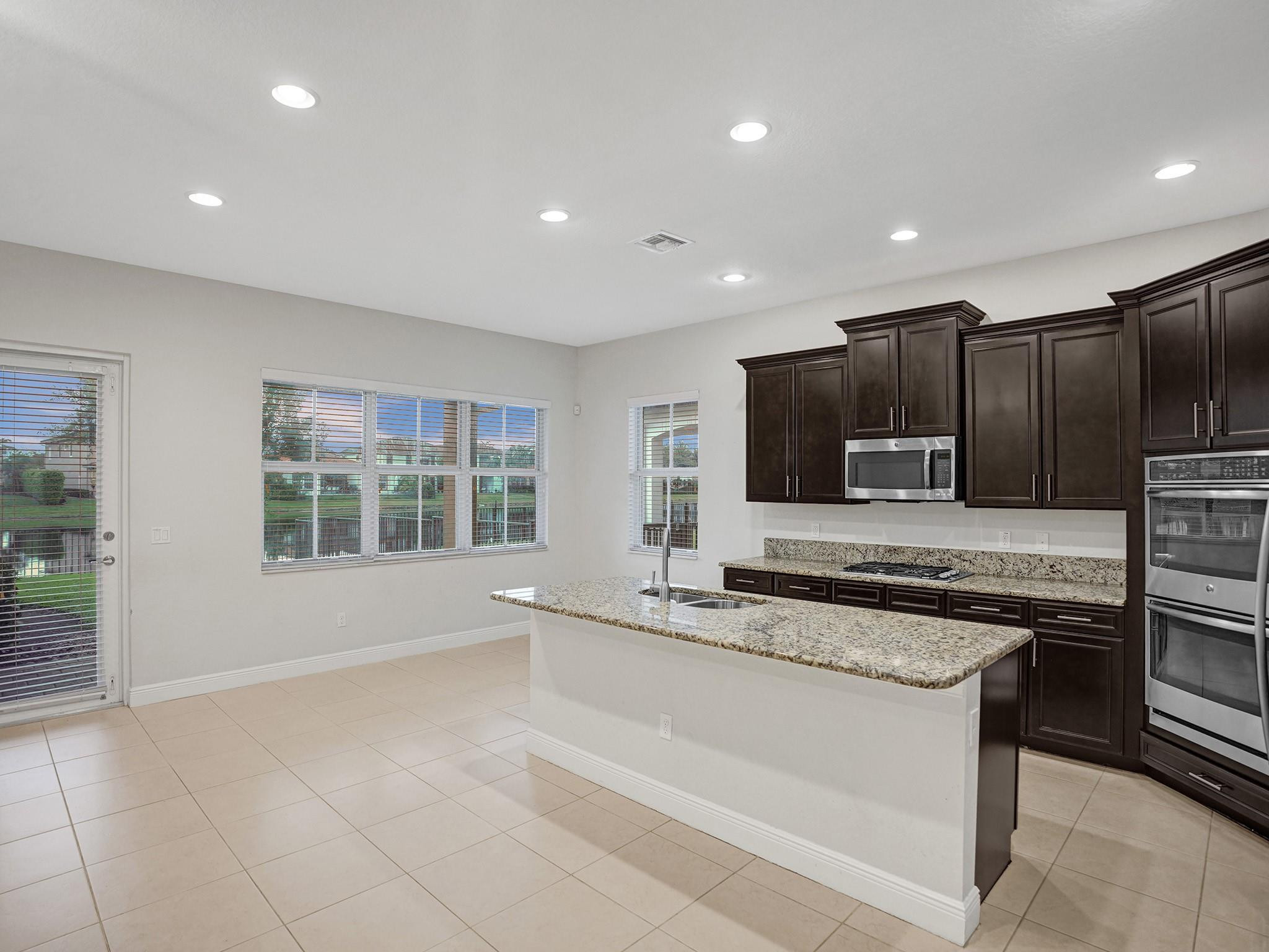 Kitchen with dark wood cabinets, granite island with sink, and stainless steel appliances.