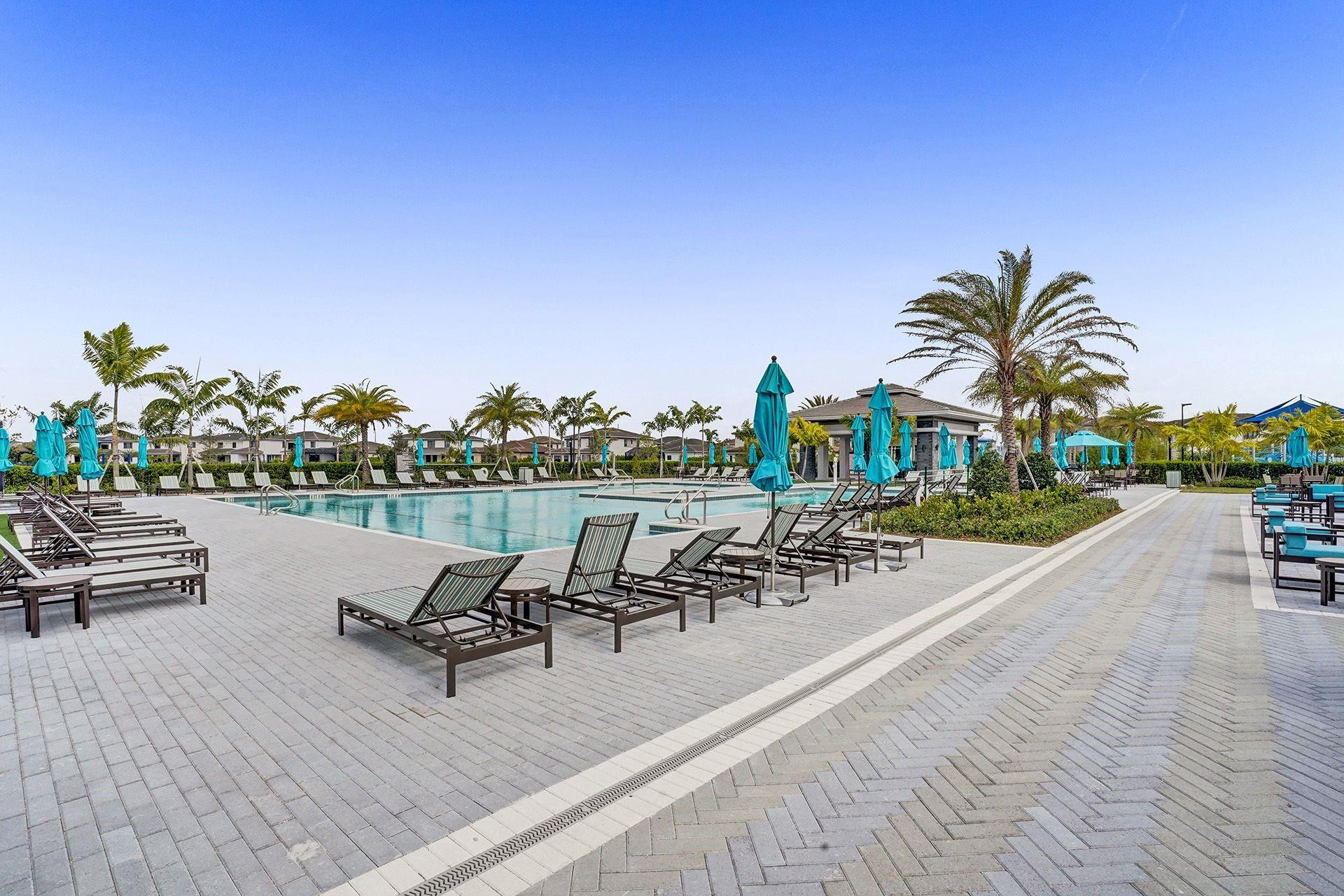 Outdoor community pool with palm trees, lounge chairs, and turquoise umbrellas.