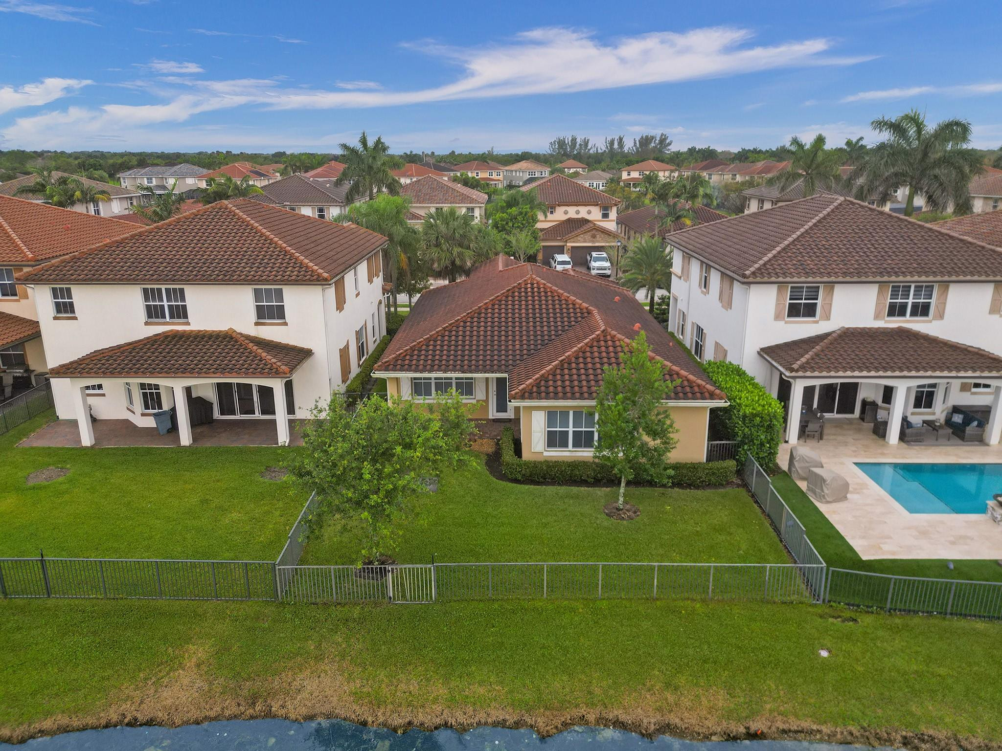 Aerial view of a tile-roofed home with a fenced lawn beside the water.
