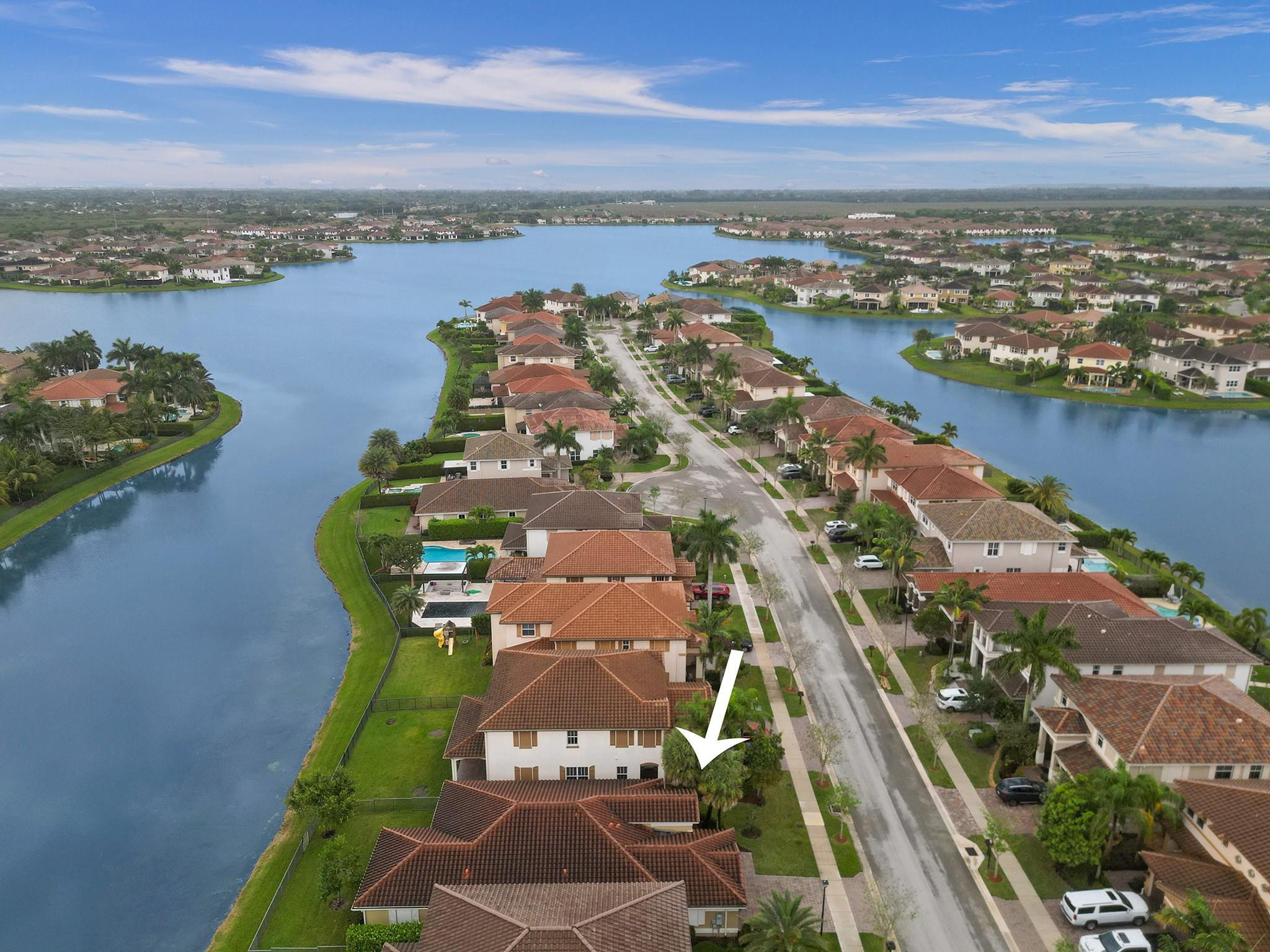 Aerial view of a lakeside neighborhood, with a white arrow pointing to a two-story house.